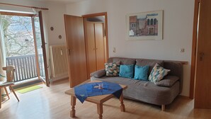 Una sala de estar con un sofá, una mesa, una silla y un ventanal corredera que da a un espacio exterior.