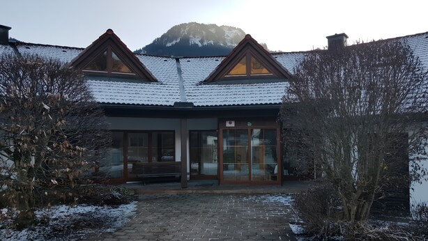 Un edificio con tejado nevado, un banco de madera y una entrada pavimentada.
