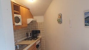 Una cocina compacta con armarios de madera, microondas, cafetera y salpicadero de azulejos.