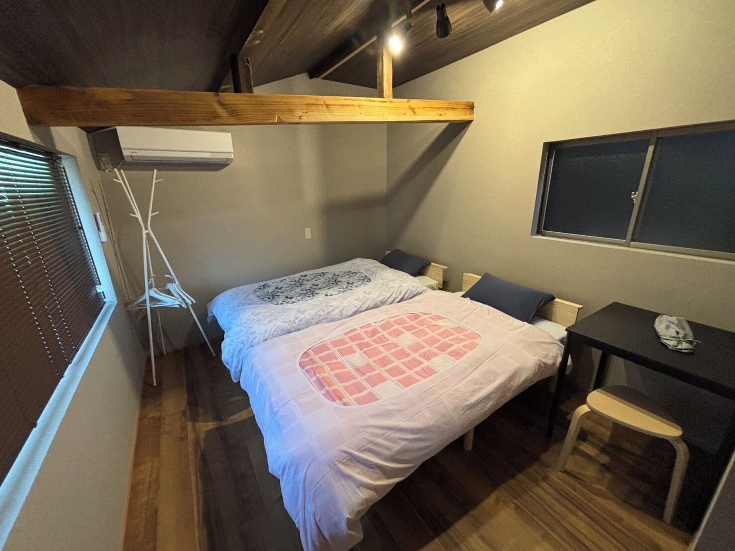Quarto com uma cama, escrivaninha, cadeira e janela com persianas.