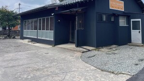 Un petit bâtiment de couleur sombre, avec une enseigne en japonais, une porte et une fenêtre.