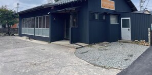 A small, dark-colored building with a sign in Japanese, a door, and a window. - Kohaku Sakaiminato (Sakaiminato)