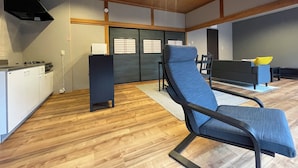 Una sala de estar moderna con un sofá azul, un sillón negro, una zona de cocina con estufa y un ventanal corredero.