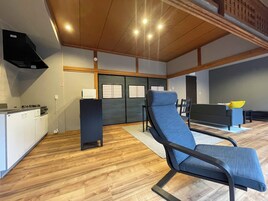 Una sala de estar moderna con un sofá azul, un sillón negro, una zona de cocina con estufa y un ventanal corredero.
