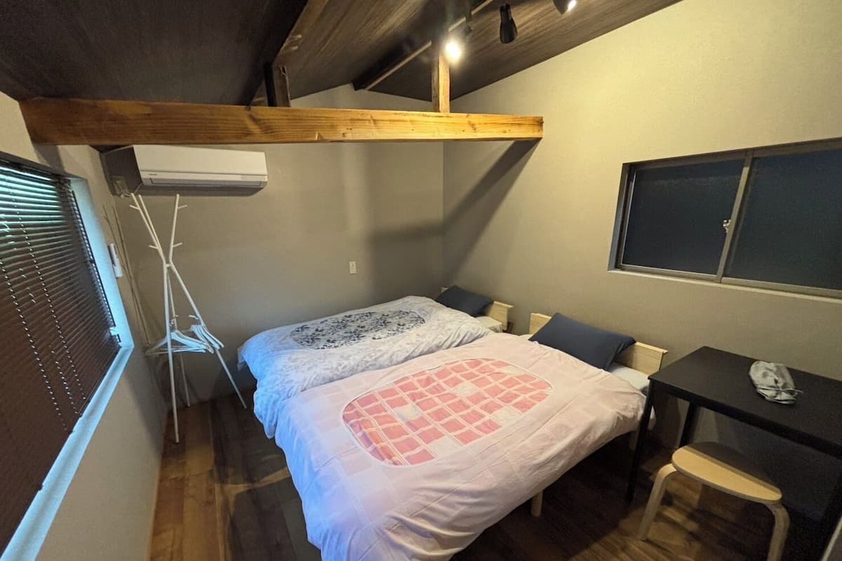 Une chambre à coucher avec un lit, un bureau, une chaise et une fenêtre avec des stores.