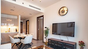 Ein modernes Wohnzimmer mit Flachbildfernseher, einem Essbereich mit rundem Tisch und Stühlen, einem Couchtisch und einem TV-Schrank.