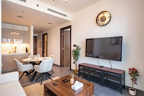A modern living room with a flat-screen TV, a dining area with a round table and chairs, a coffee table, and a TV stand. - Premium 1BR Plus Study Canal View Near Downtown (Dubai)