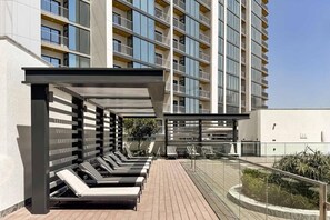 A modern building with a rooftop deck featuring sun loungers and a covered seating area. - Premium 1BR Plus Study Canal View Near Downtown (Dubai)
