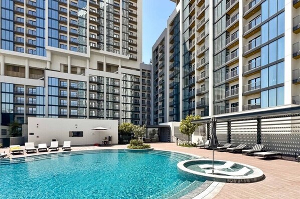 A modern apartment building with a swimming pool, lounge chairs, and a sun terrace. - Premium 1BR Plus Study Canal View Near Downtown (Dubai)