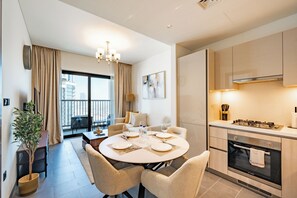 A modern kitchen with a built-in oven, a dining area with a round table and chairs, and a view of the city through large windows. - Premium 1BR Plus Study Canal View Near Downtown (Dubai)
