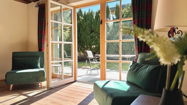 A room with a green sofa, a chair, a lamp, and a view through large glass doors to an outdoor seating area. - The cozy Mountain Suites 1& 2 in a fantastic location in Reith near Kitzbühel (Kitzbühel)