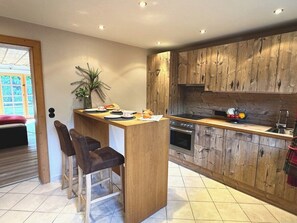 Eine moderne Küche mit Holzausstattung, einer zentralen Kochinsel, Barhocker und einem Essbereich mit Pflanze.