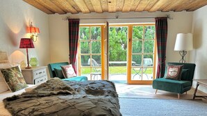 A bedroom with a large bed, a green armchair, a wooden ceiling, and a view through a glass door. - The cozy Mountain Suites 1& 2 in a fantastic location in Reith near Kitzbühel (Kitzbühel)
