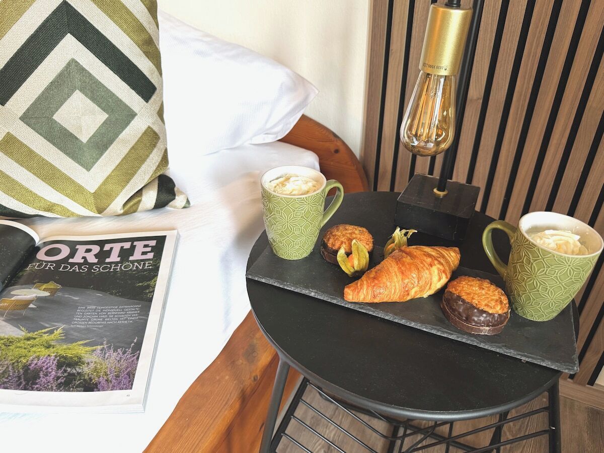 A bed with a pillow, a magazine, a tray with pastries, and a table lamp.