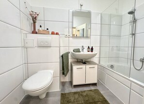 Une salle de bain moderne équipée de toilettes, d’un lavabo, d’un miroir, d’une douche et d’un tapis vert.