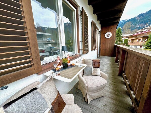 A wooden deck with a table and chairs, a clock, and a view of buildings and mountains. - Stylish design apartment for 3-4 people in the heart of Kitzbühel (Kitzbühel)