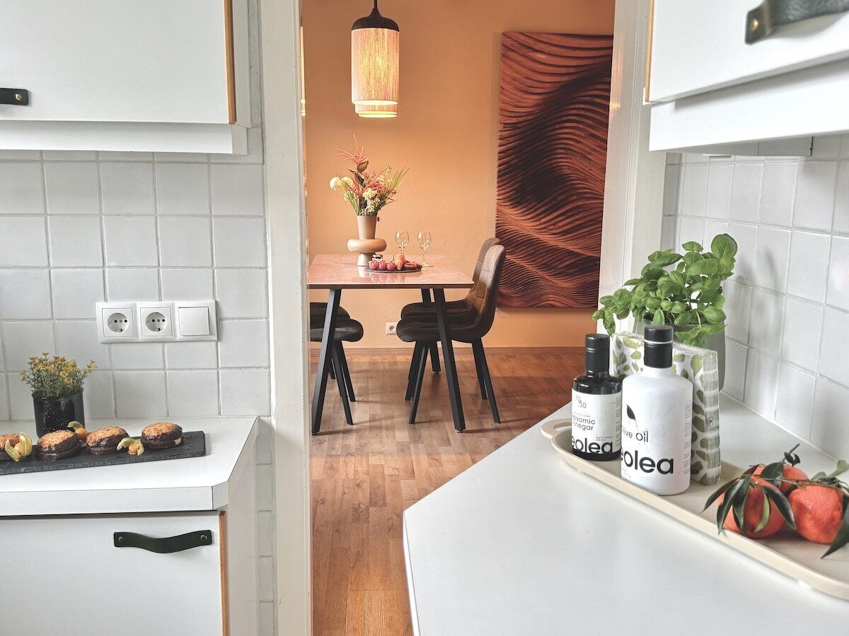 A kitchen with white cabinets, a dining area with a table and chairs, and a hanging light fixture.