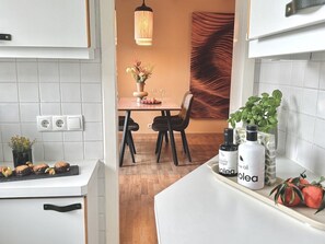 Une cuisine avec des meubles blancs, un coin repas comprenant une table et des chaises, et un luminaire suspendu.