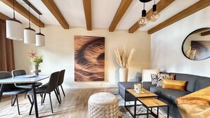 Uma sala de estar moderna com área de jantar, vigas de madeira, luminárias pendentes e um quadro abstrato grande.