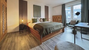 Quarto com cama de madeira, uma mesinha, uma cadeira e janela com cortinas.