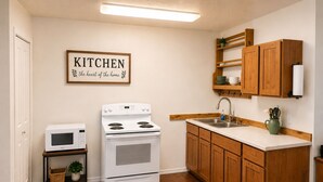 Una cocina con estufa, microondas, lavabo, armarios de madera y un cartel que dice 'KITCHEN the heart of the home'.