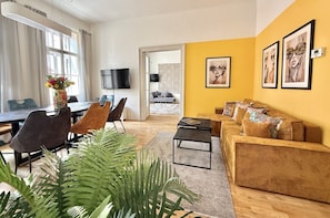 Ein Wohnzimmer mit einer Couch, einem Couchtisch und Sesseln, ein Essbereich mit Tisch und Stühlen sowie ein an der Wand befestigter Fernseher.