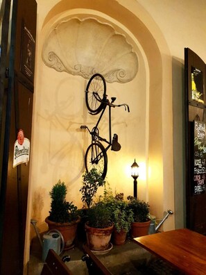 Ein an der Wand befestigtes Fahrrad, Blumentöpfe, ein Holztisch und ein Schild mit einer Biersorte.