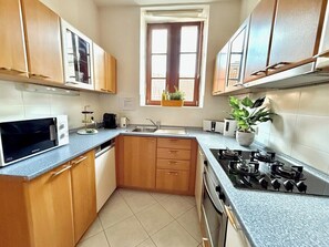 A compact kitchen with wooden cabinets, a microwave, a sink, a stove, and a window with a view. - Style & Design No. 1 City Centre Prag Style & Design No. 1 City Centre Prag (Praha 1)