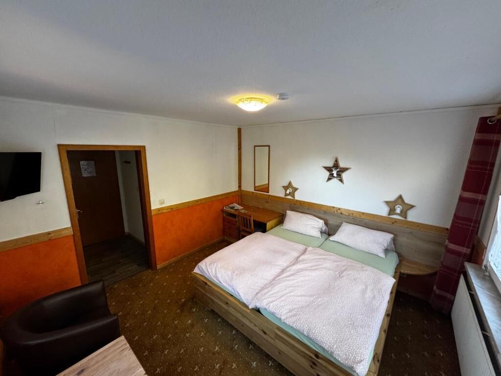 A single-bed room with a wooden headboard, a bedside table, a mirror, and a wall-mounted star decoration.