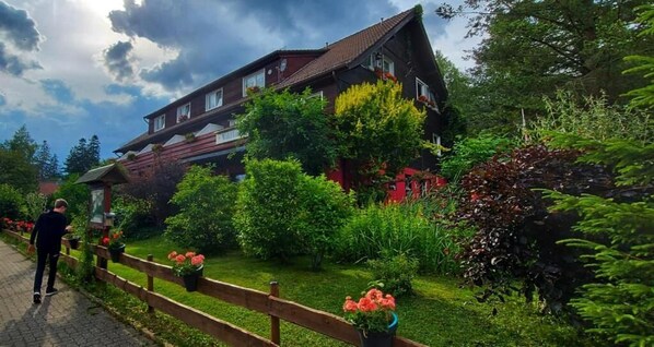 A house with a sloped roof, surrounded by lush greenery and a wooden fence. - Waldlandhaus (Goslar)