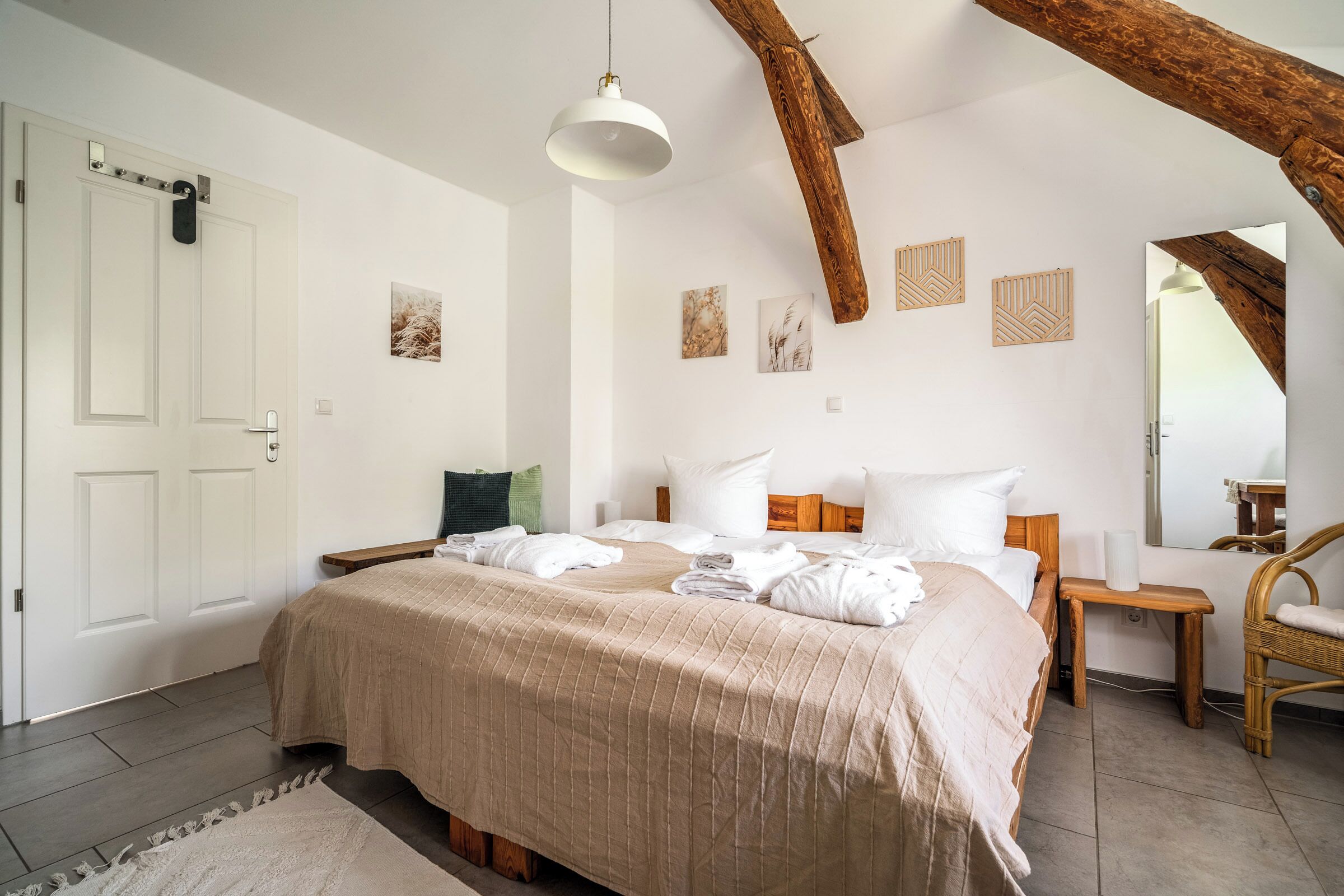 Un dormitorio con una cama, una silla de madera, una mesita de noche y un espejo.