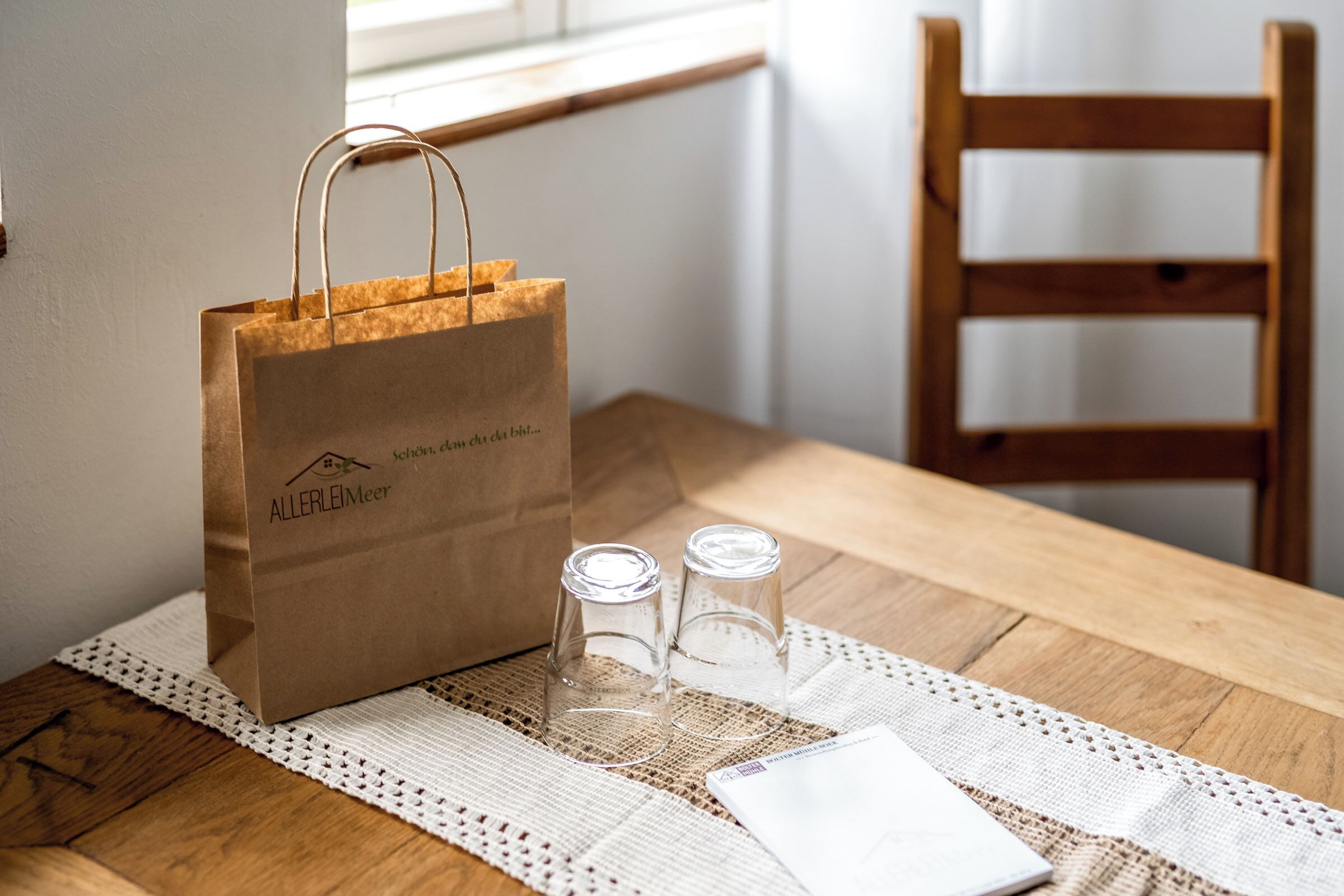 Una mesa de madera con una bolsa de papel, dos vasos transparentes y un servilleta blanca.