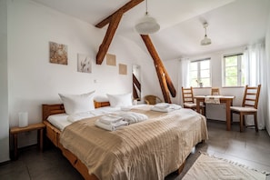 A bedroom with a large bed, wooden beams, a desk, and chairs.