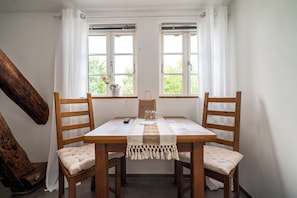 A dining table with two chairs, a wooden bench, a table runner, and a window with curtains.