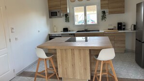Une cuisine moderne avec des meubles en bois, un îlot central, deux tabourets de bar, un four à micro-ondes encastré et un réfrigérateur en acier inoxydable.