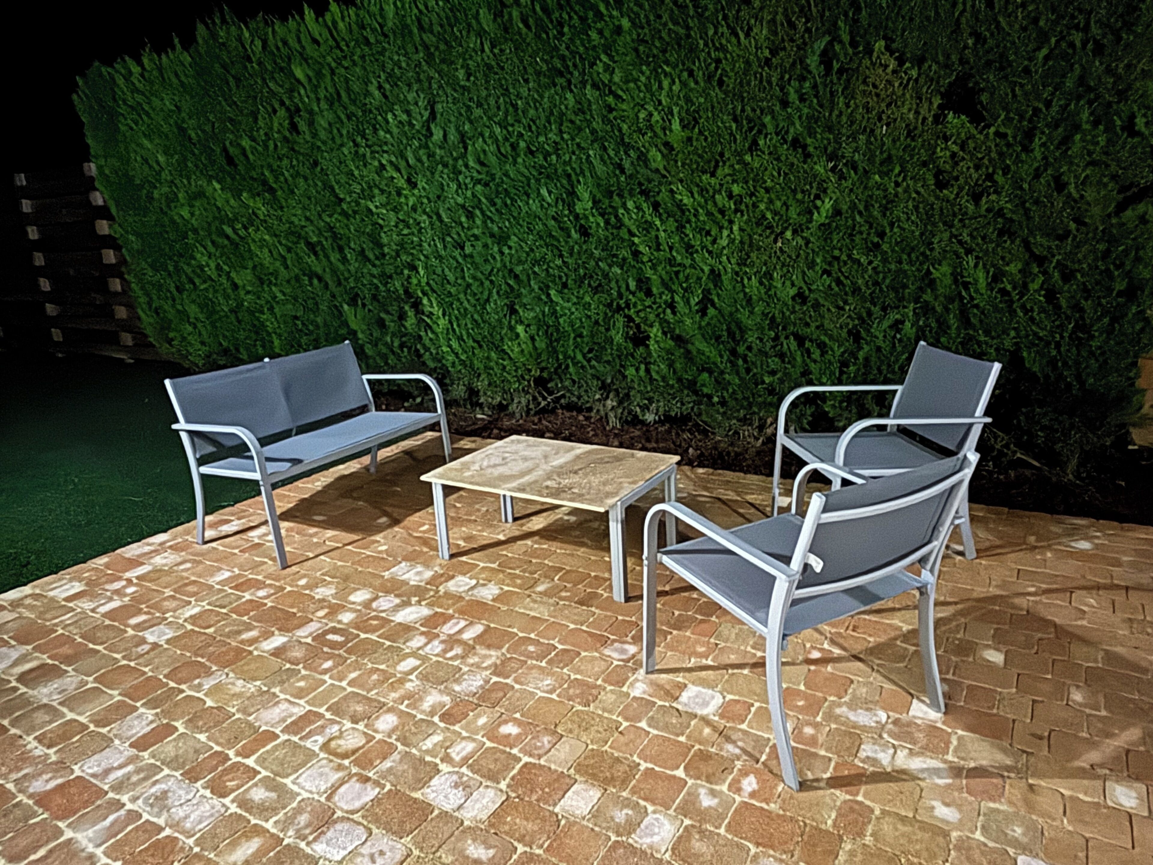 Un espace extérieur aménagé avec des sièges, doté d’un sol en briques, de deux chaises en métal et d’une table en bois.