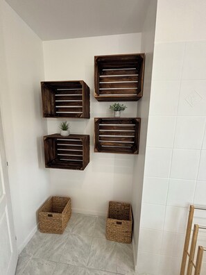 Rincón con dos repisas de madera contra una pared blanca, cada una sosteniendo una pequeña planta en maceta.