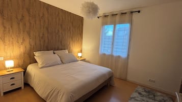 A bedroom with a wooden headboard, a bed with white bedding, two bedside tables with lamps, and a window with curtains.