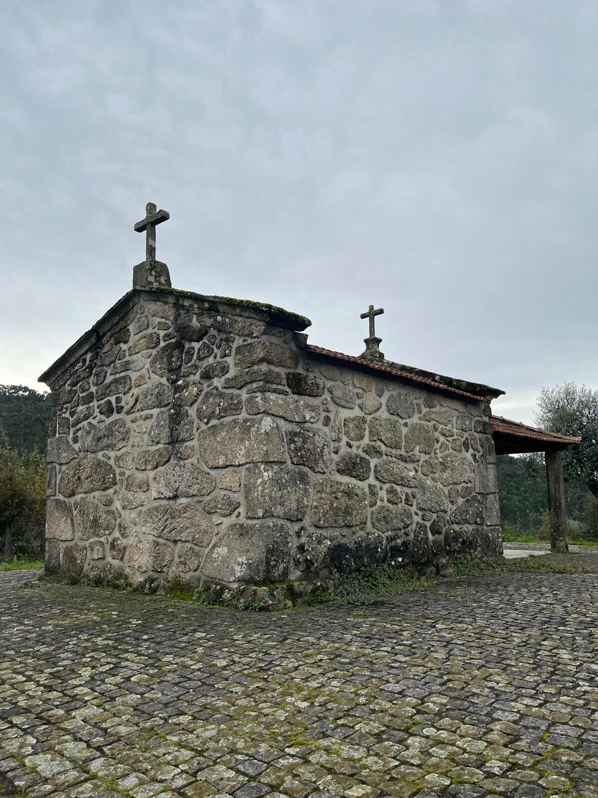 Un pequeño edificio de piedra con dos cruces en la parte superior, techo de tejas y suelo adoquinado.