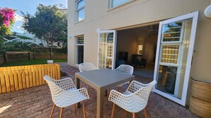 Un patio con una mesa y sillas, un banco de madera y una puerta corrediza de vidrio que da a una habitación interior.