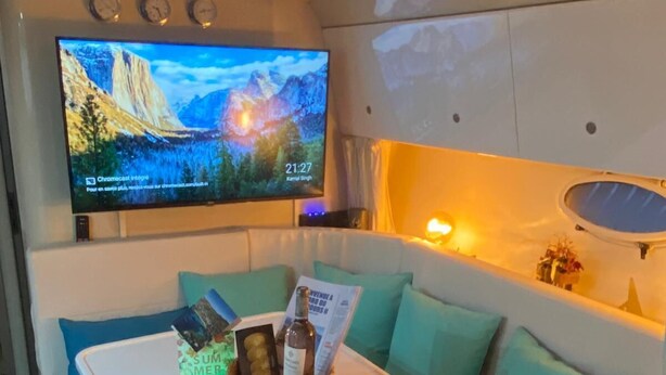 Ein gemütliches Interieur mit Fernseher, der eine schöne Landschaft zeigt, einem kleinen Tisch mit Snacks und einer bequemen Sitzecke mit Kissen.