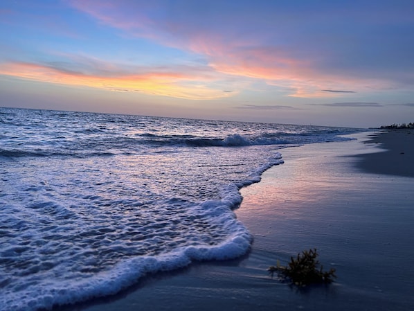 A beach with waves approaching the shore, a clear sky, and a distant horizon.