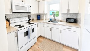 Moderni keittiö, jossa on valkoiset kaapit, sisäänrakennettu mikroaaltouuni, liesi ja pesuallas.