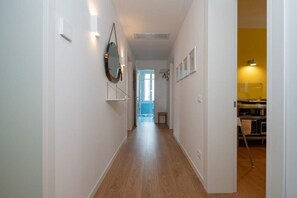 A hallway with wooden flooring, white walls, and a door leading to a room with a yellow wall and a kitchen area. - Charming Venetian  Retreat-3 Bedrooms, Dorsoduro (Venezia)