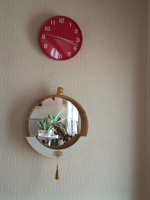 Eine rote Wanduhr und ein runder Spiegel mit Holzrahmen.