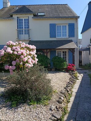 Ein zweigeschossiges Haus mit einem Schotterweg, einer Veranda und einem Garten mit rosa Blumen.