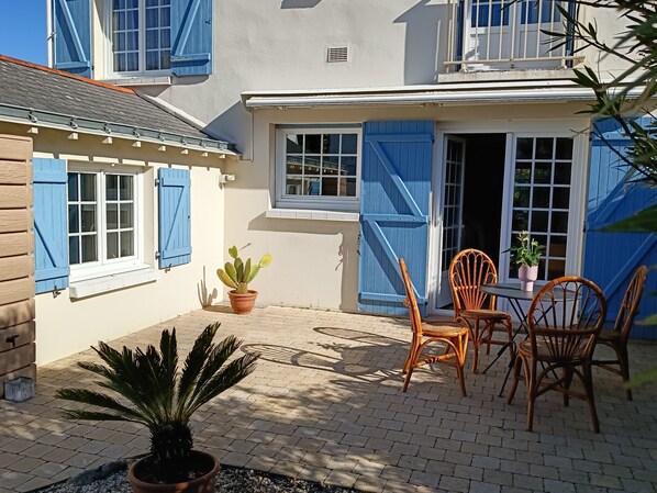 Eine Terrasse mit Tisch und Stühlen, einem Blumentopf und einem Gebäude mit blauen Fensterläden.