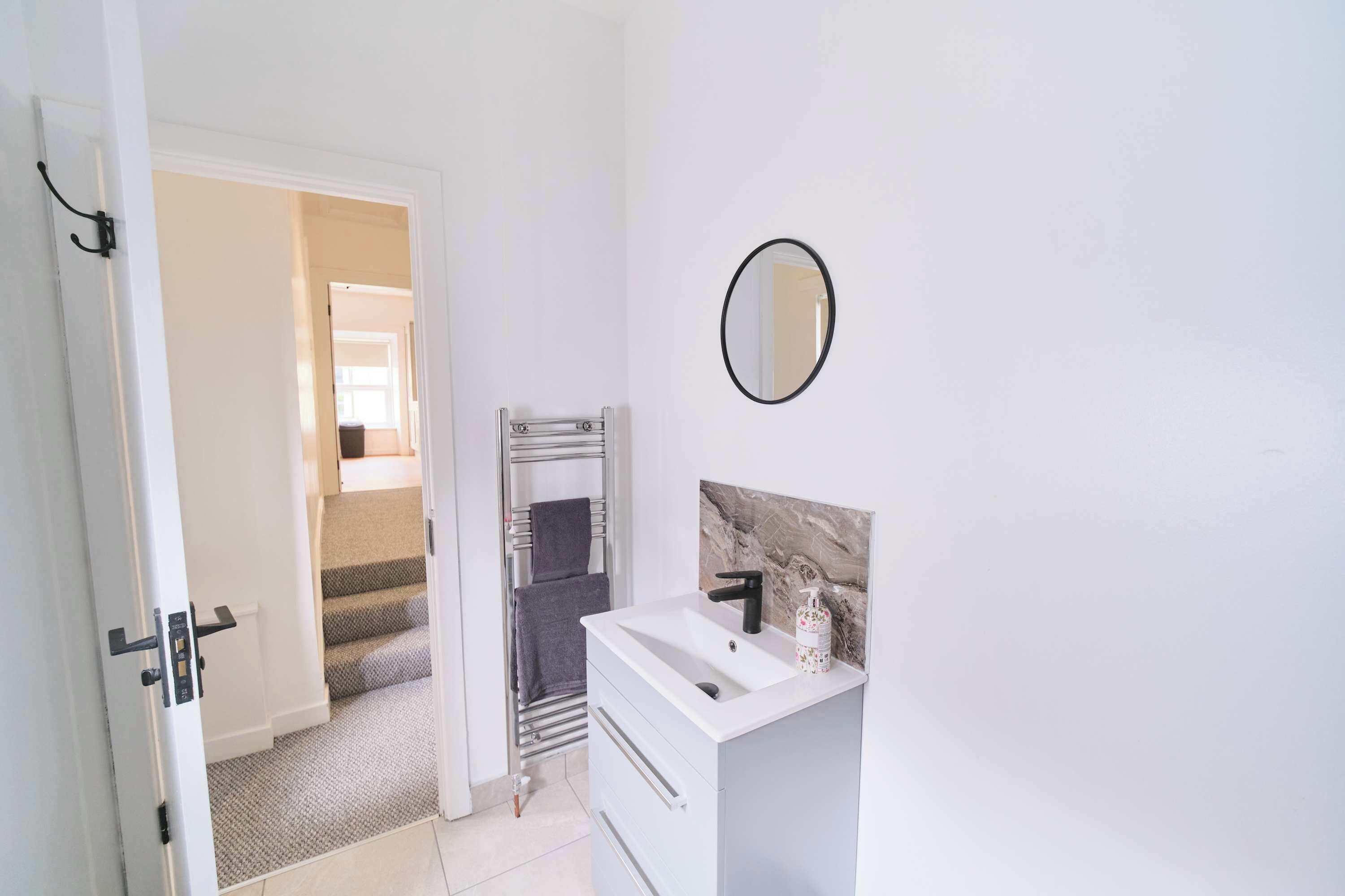 Un bagno con un lavandino bianco, uno specchio e un portasciugamani.