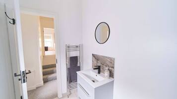 Un bagno con un lavandino bianco, uno specchio e un portasciugamani.
