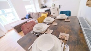 Una tavola imbandita con piatti, ciotole e posate, un divano e una cucina sullo sfondo.